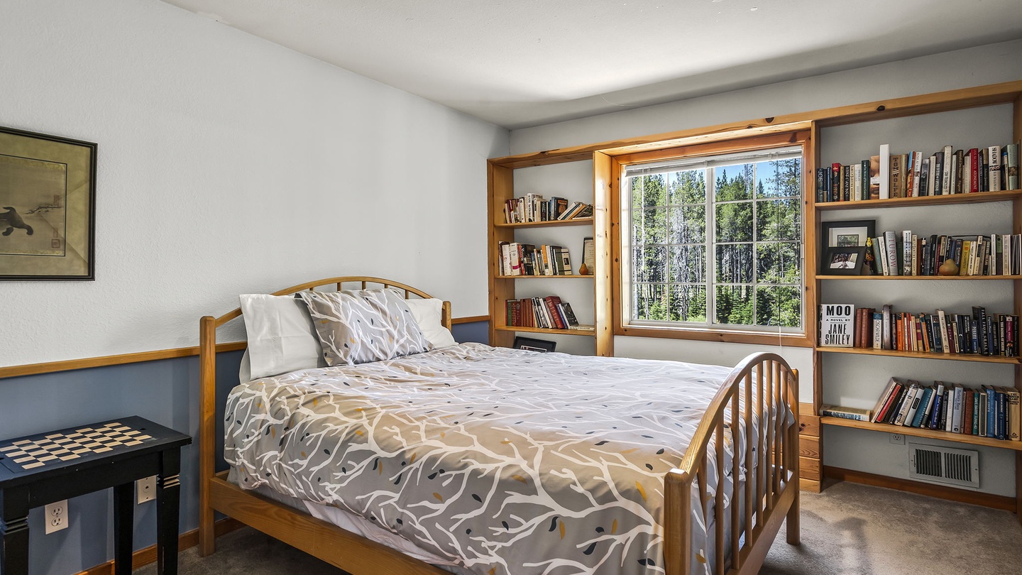Curl up with a good book in your cozy bedroom, where built-in shelves frame a peaceful forest view and sunlight streams through the window.