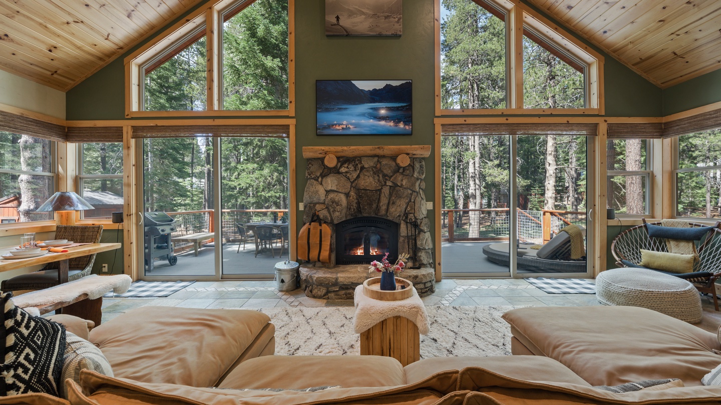 Sink into plush seating by a crackling stone fireplace, surrounded by soaring windows that frame towering pines and lead you out to your private deck. This inviting space blends cozy warmth with breathtaking forest views.