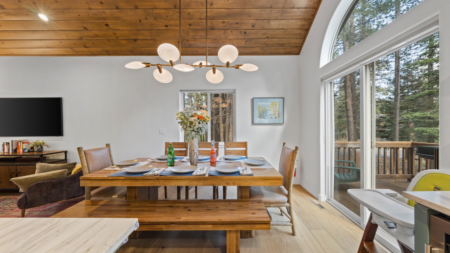 Gather around the warm wood table under vaulted ceilings where natural light pours through soaring windows. Your peaceful forest retreat awaits just beyond the balcony.