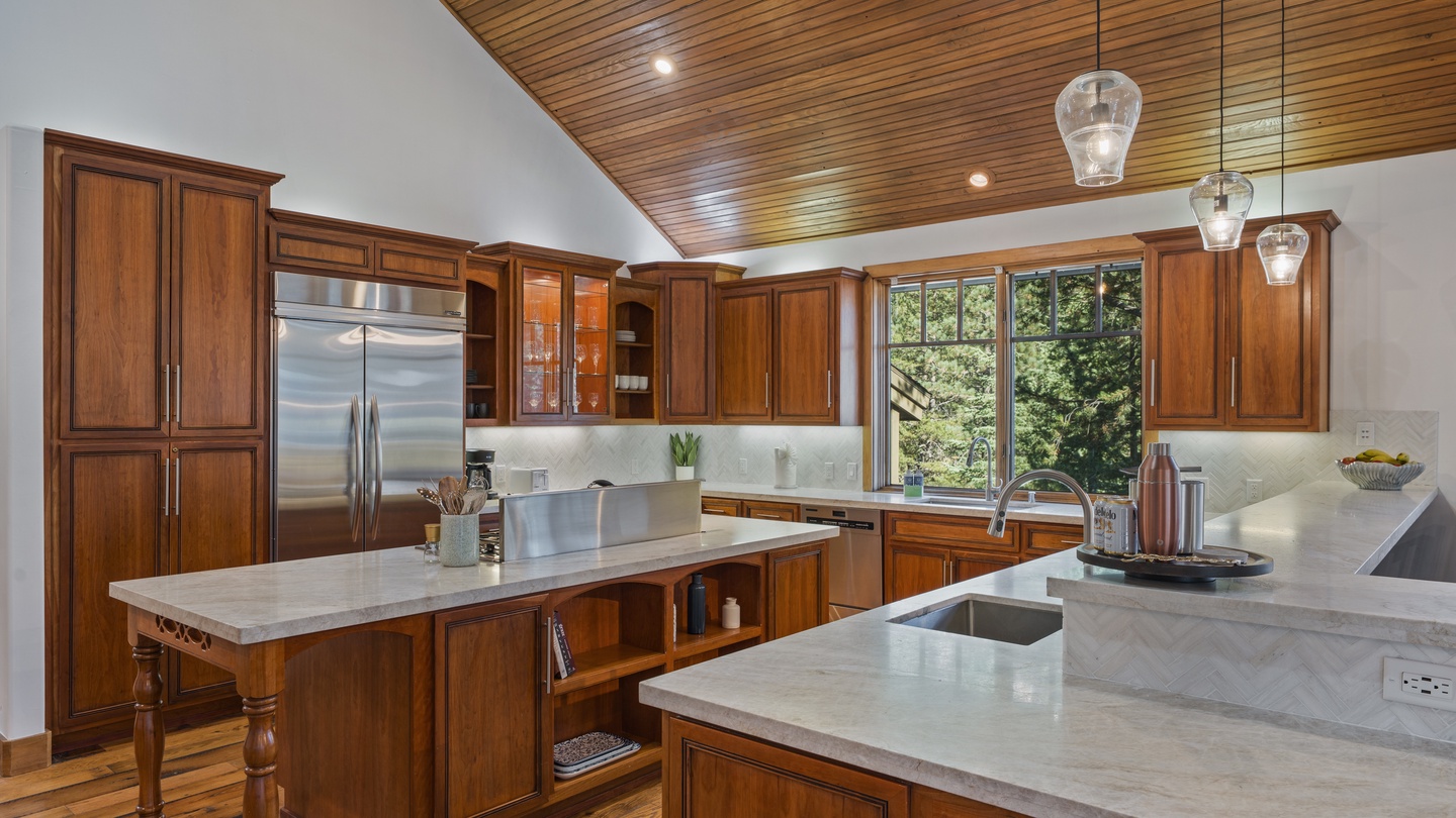 Your gourmet kitchen awaits with rich wood cabinetry, sleek marble countertops, and modern stainless steel appliances. Large windows frame peaceful garden views while pendant lighting adds warmth overhead.