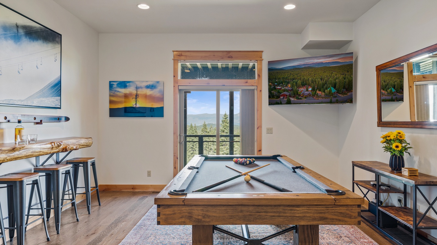 Your game room awaits with a handsome pool table and stunning mountain views through the glass door. Natural wood accents and bright natural light create the perfect atmosphere for friendly competition and relaxation.