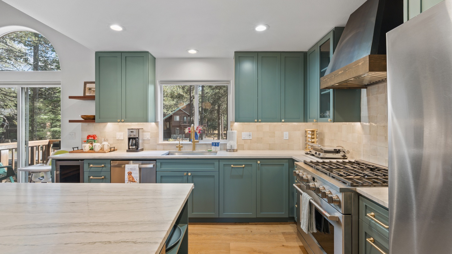 Your fully equipped kitchen features sage-green cabinetry, stainless appliances, and views of the surrounding pines through large windows—a chef's dream nestled in nature.