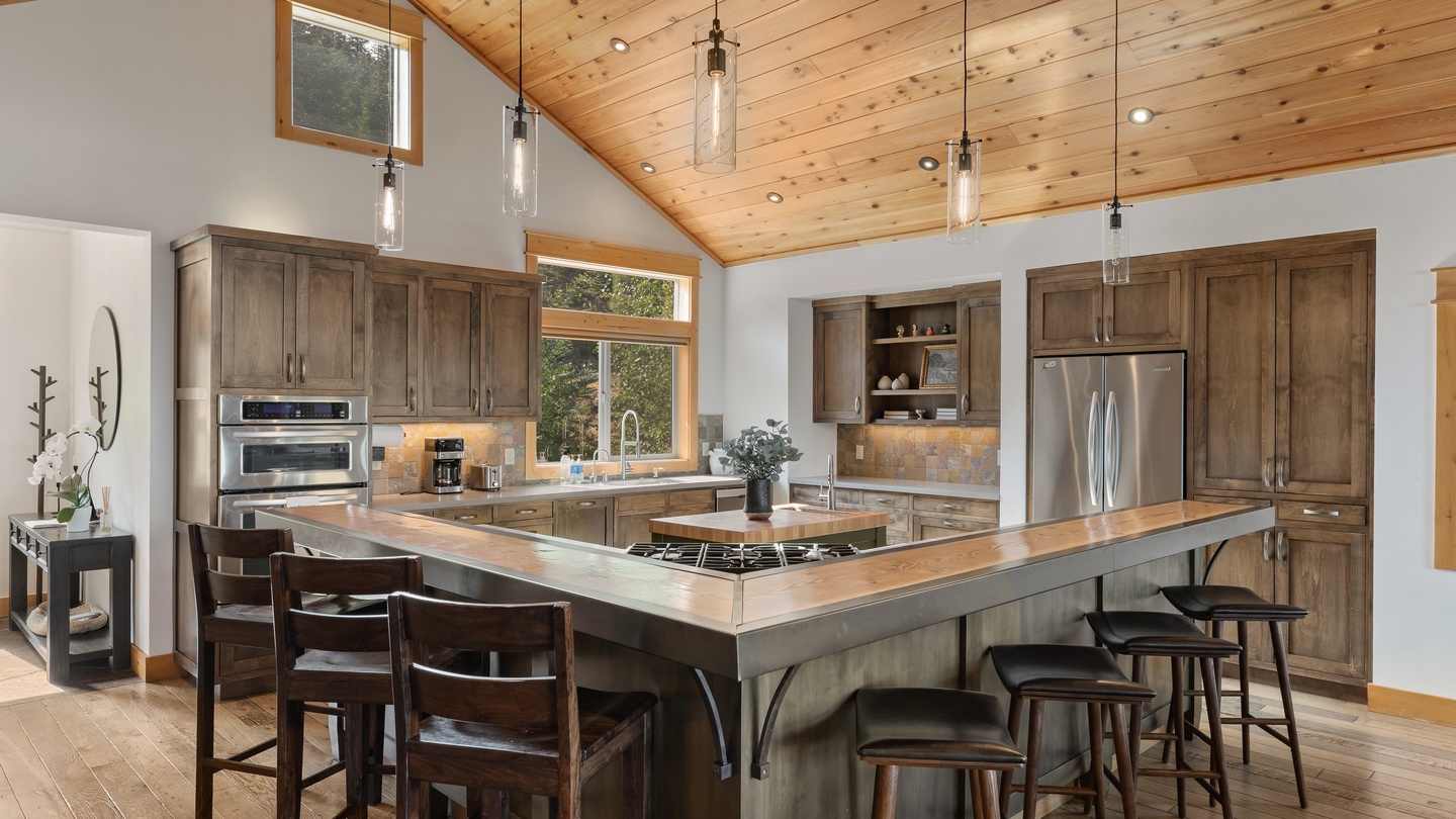 Gather around the spacious island where natural wood tones meet modern convenience. Your group can cook, chat, and connect beneath vaulted ceilings that fill the space with warmth and light.