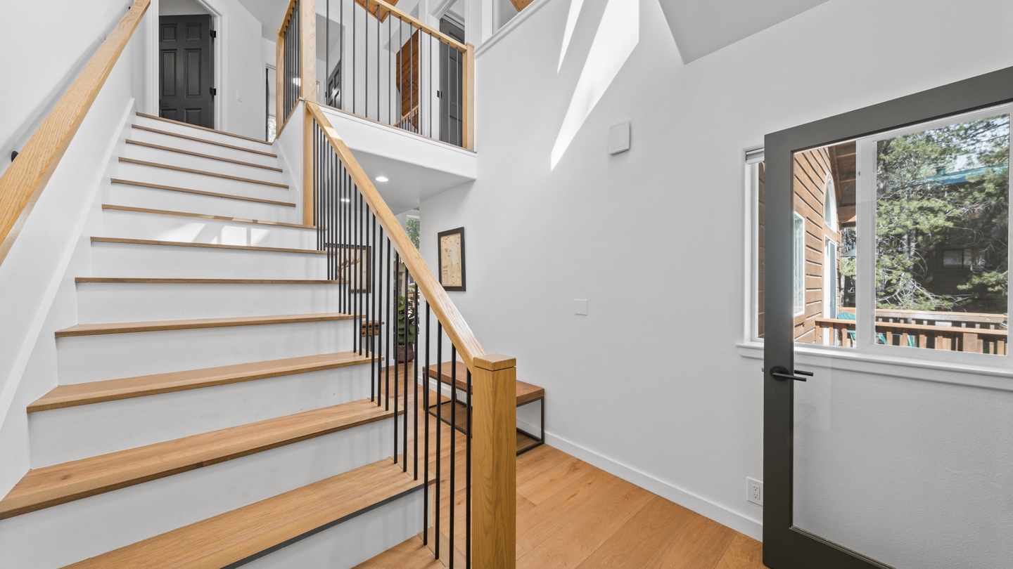 Natural light floods the open stairway, highlighting warm wood tones and cathedral ceilings that make this space feel bright and inviting.