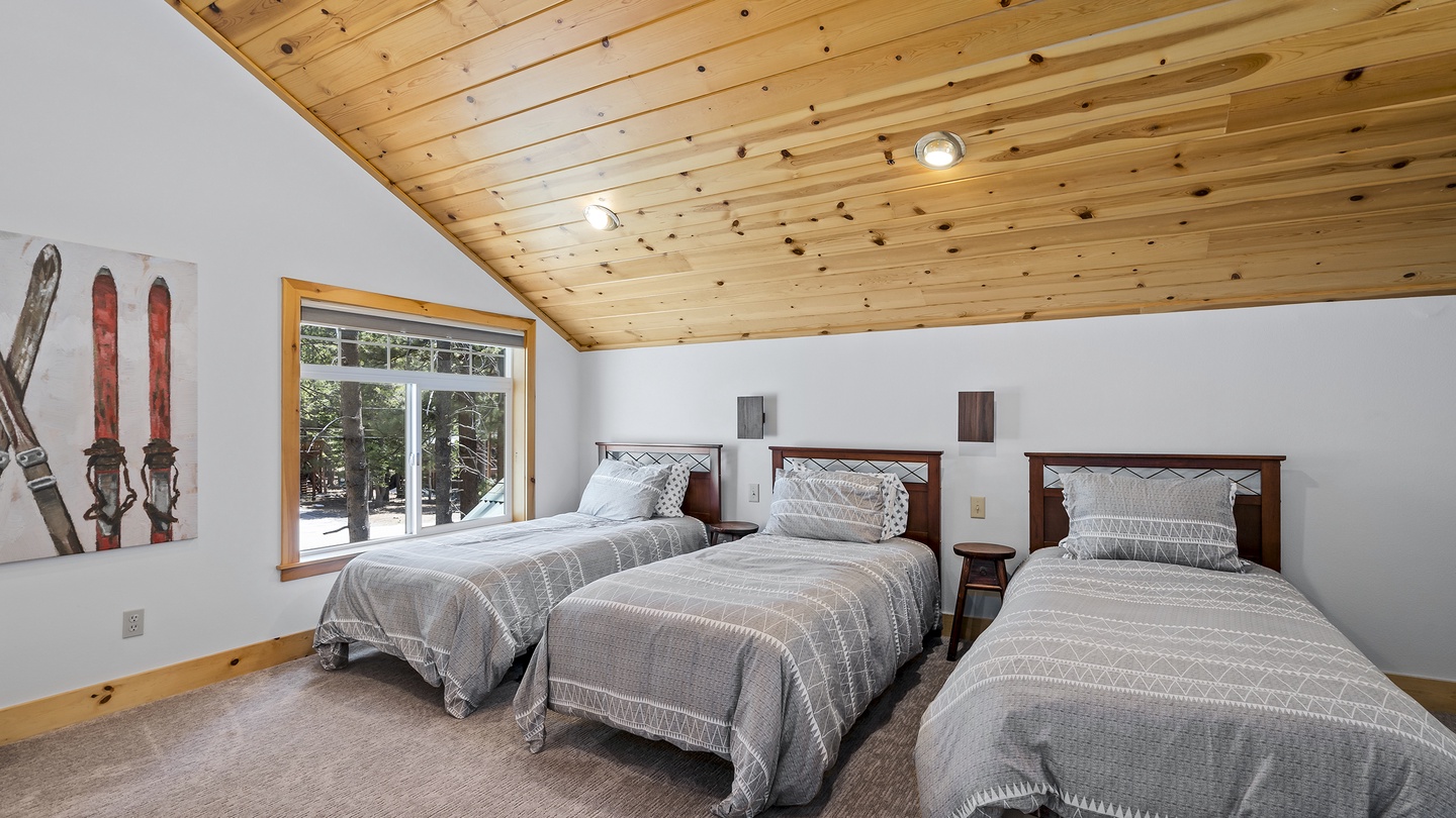 Drift off under the warm glow of rustic wood ceilings, with three cozy beds ready to cradle your group after a day of mountain adventures. Natural light filters in, framing snowy forest views.