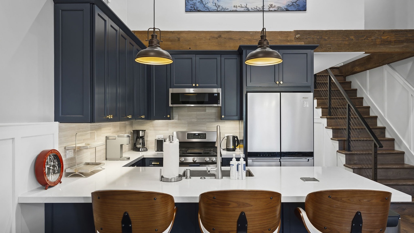 Your modern kitchen invites culinary creativity with sleek navy cabinets, gleaming white counters, and warm pendant lighting creating the perfect cooking atmosphere.
