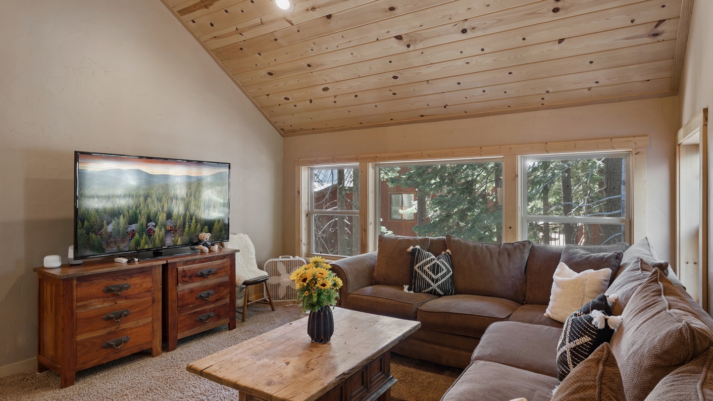 Sink into plush seating beneath natural wood ceilings and gather with loved ones in this warm, light-filled living space. Large windows frame forest views, creating a peaceful mountain retreat.