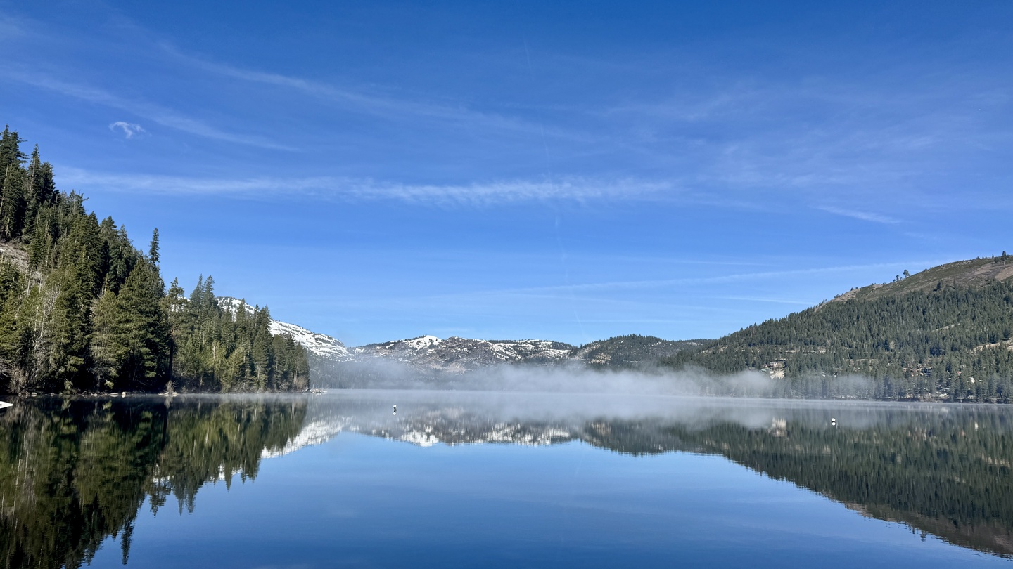 Donner Lake Spring time mirrors snow-capped peaks and forest-lined shores beneath brilliant blue skies in this serene natural setting.