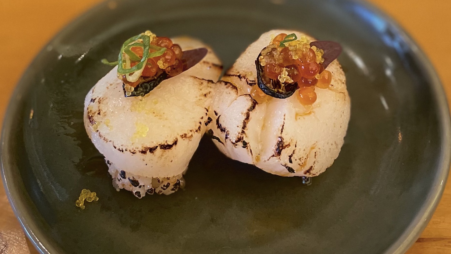 Savor expertly prepared seared scallops topped with vibrant caviar, beautifully plated for your culinary delight.