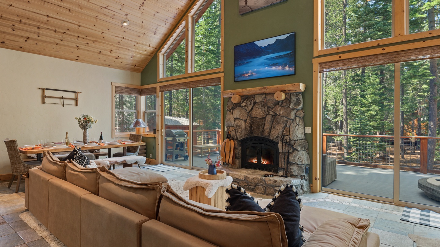 Sink into comfort in this open great room where natural light pours through soaring windows framing lush forest views. The stone fireplace adds cozy warmth, perfect for unwinding after exploring the outdoors.