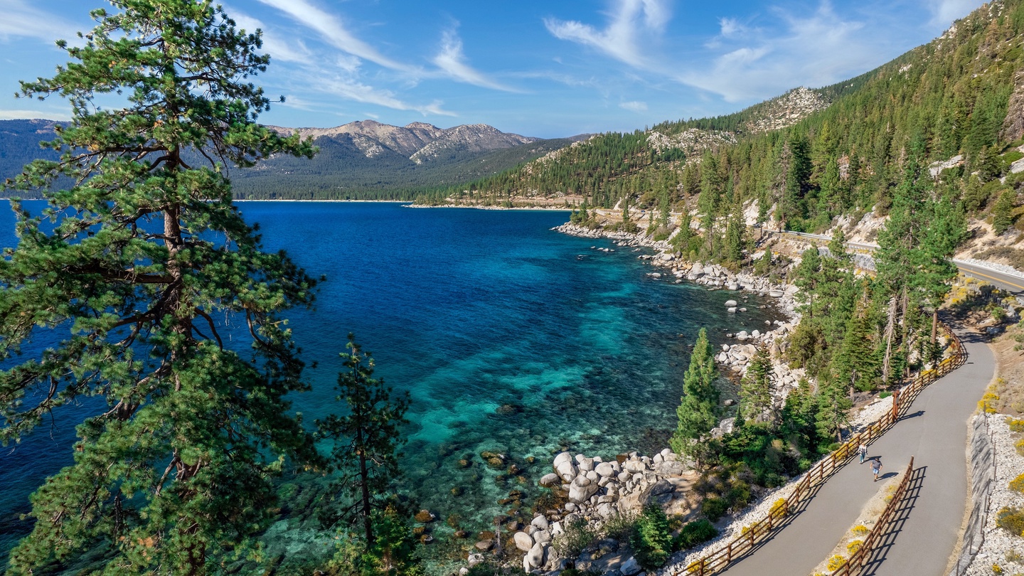 Stunning alpine lake framed by forested mountains and scenic roadway, defining the natural beauty of the surrounding area.