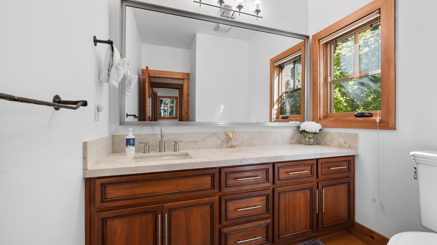 Your elegant bathroom features rich wood cabinetry, gleaming marble countertops, and natural light streaming through the windows, creating a warm and refreshing retreat.