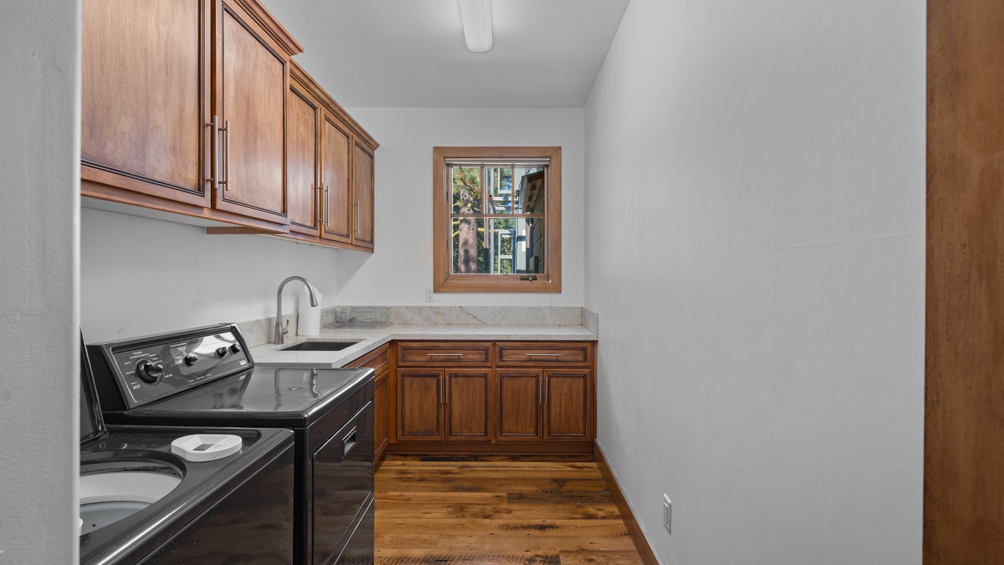 Your private laundry room features warm wood cabinetry, a deep sink, and plenty of storage—making chores feel less like work in this bright, organized space.