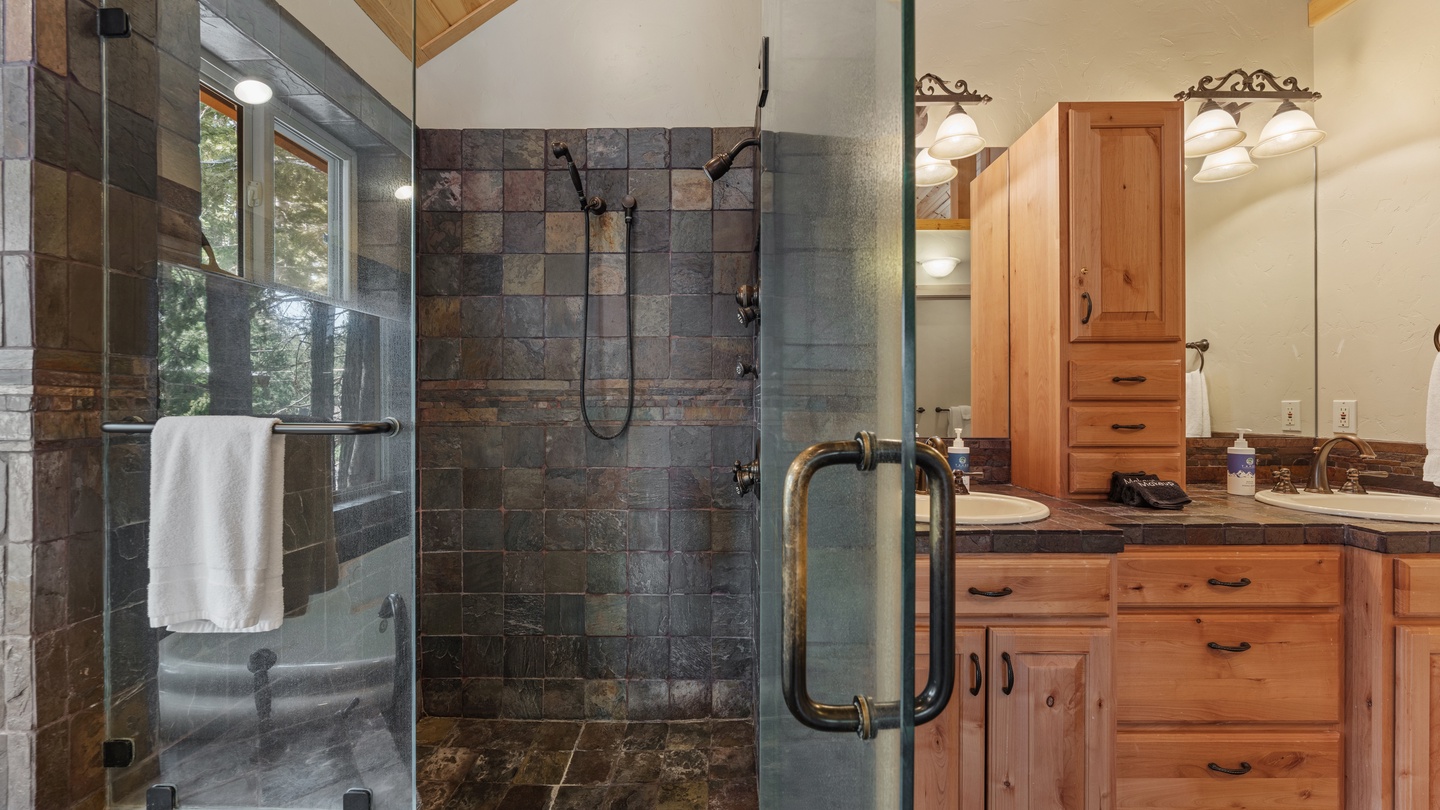 Unwind in your private spa-like bathroom with a spacious walk-in shower featuring natural slate tile and views of the surrounding forest through the glass enclosure.