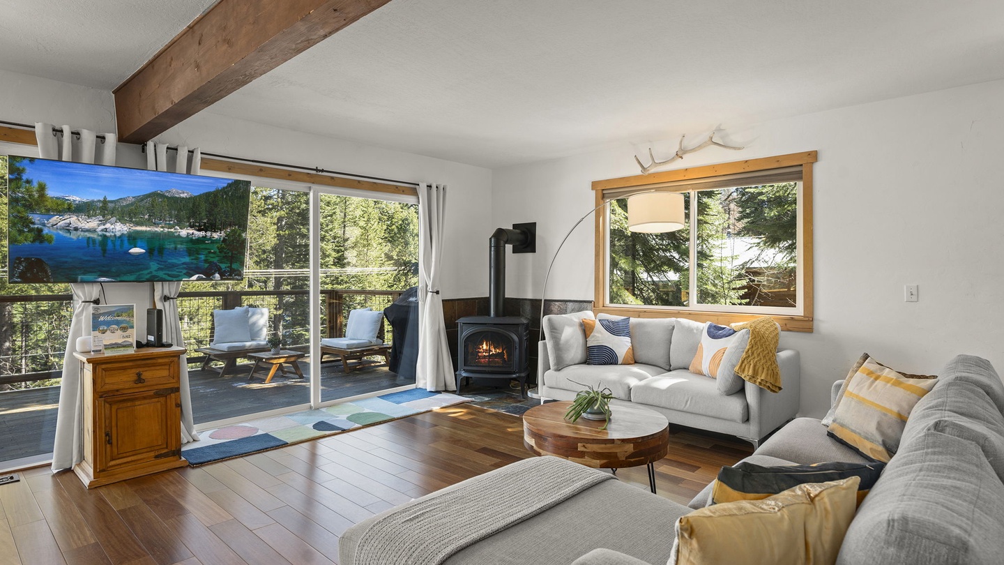 Unwind in your cozy living room with exposed beams, crackling fireplace, and forest and lake views through panoramic windows.