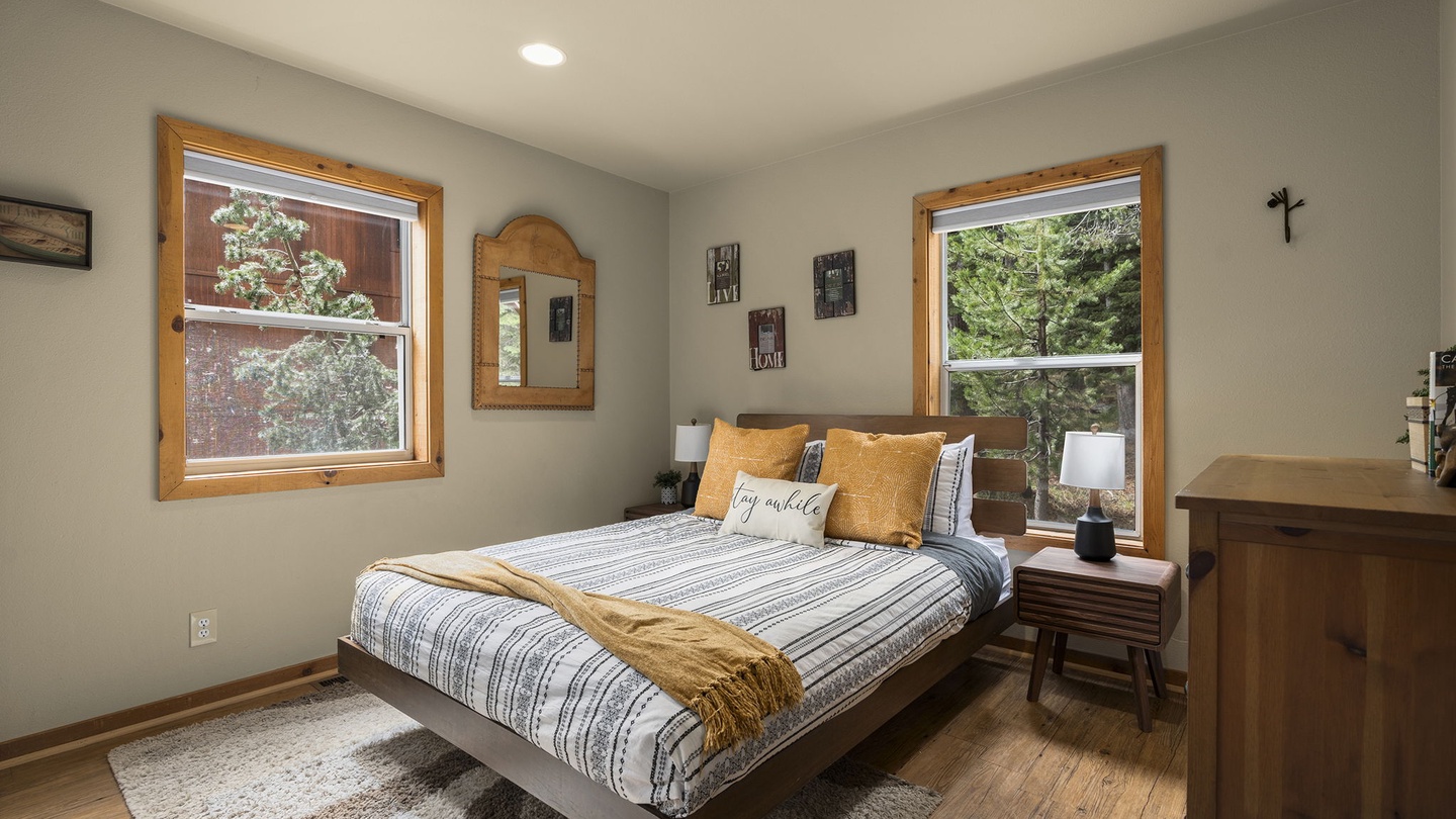 Sink into your comfortable bed surrounded by warm wood accents and natural light from dual windows overlooking lush greenery.