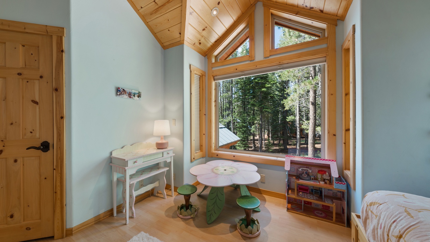 Step into your child's bright forest retreat, where soaring wood-beamed ceilings and floor-to-ceiling windows frame a peaceful view of tall pines, filling the room with natural light and inviting the outdoors in.