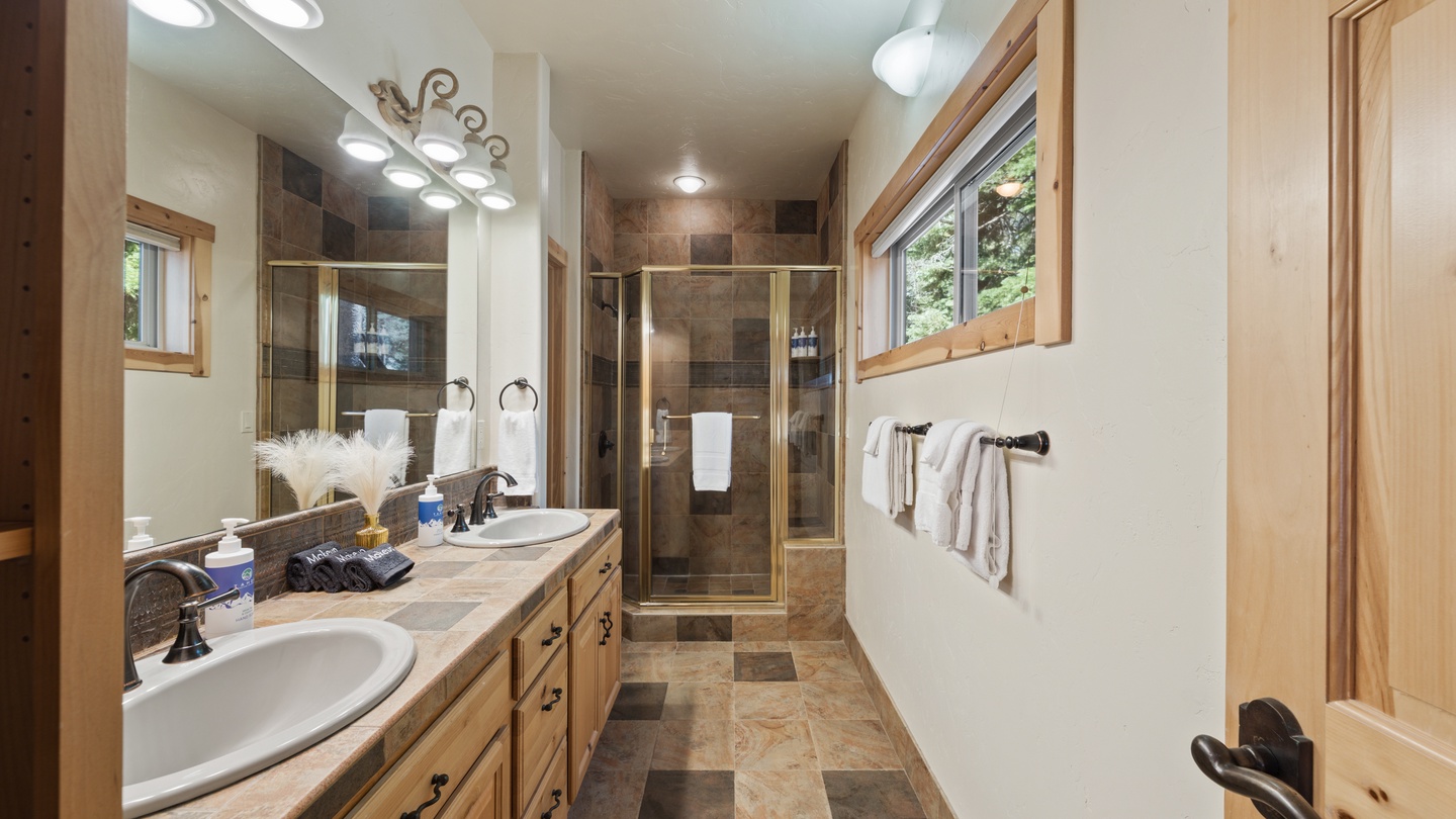 Step into your private spa-like retreat with dual vanities, elegant stone tile, and a spacious walk-in shower framed by natural wood accents and warm lighting.