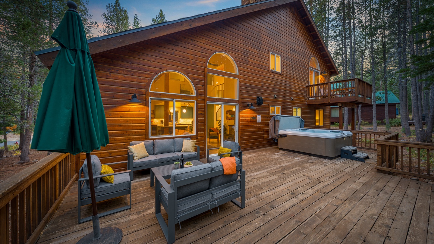 Your peaceful mountain retreat welcomes you with a spacious deck featuring comfortable lounge seating and a private hot tub, perfect for soaking under the trees as evening lights glow warmly from within.