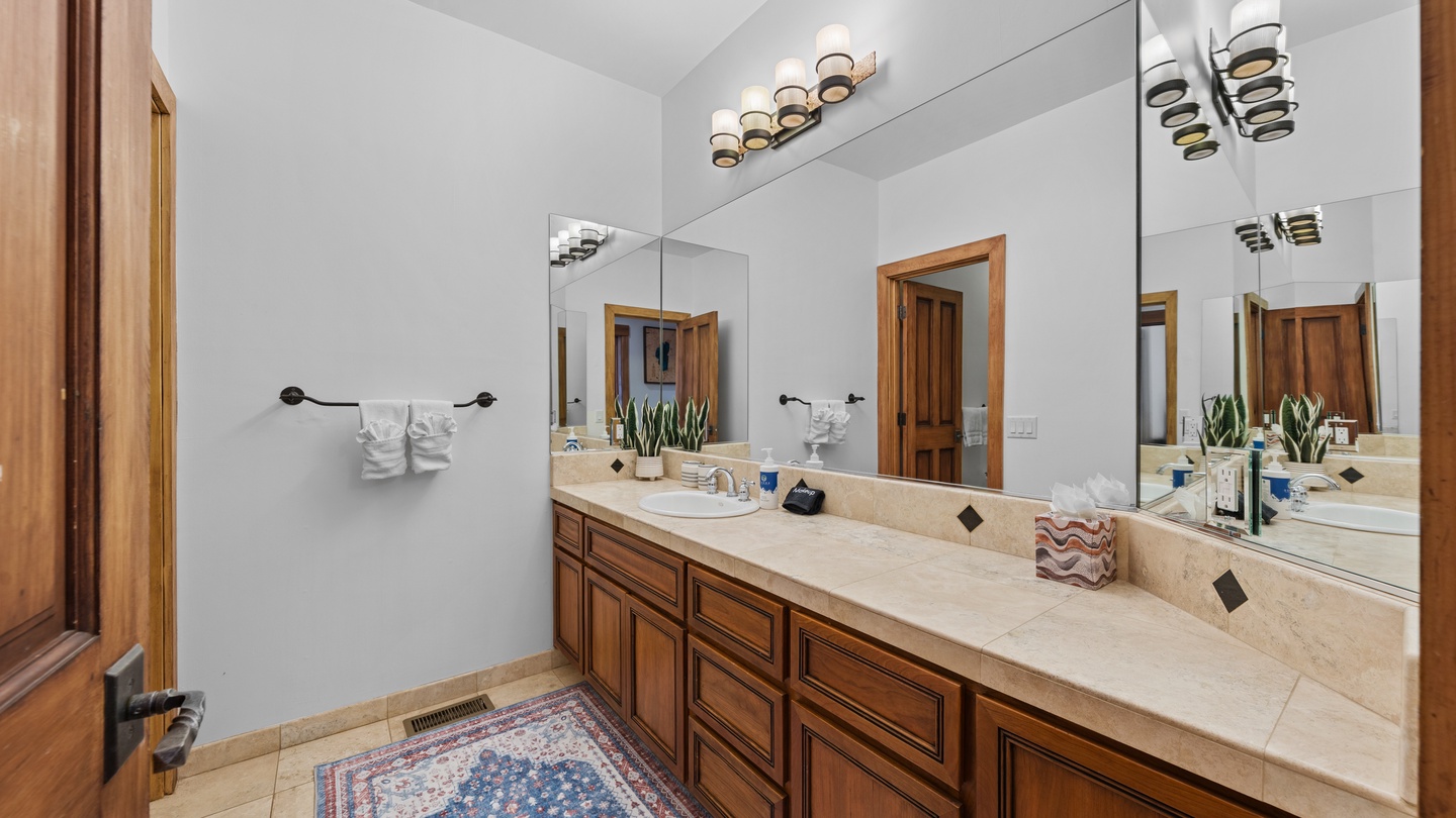 Your spacious bathroom features a beautifully crafted dual-sink vanity with elegant stone countertops, warm wood cabinetry, and modern lighting, creating a comfortable and inviting space to start your day.