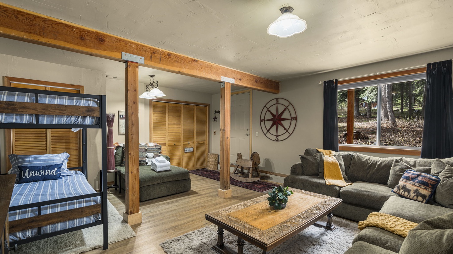 Relax in your spacious living room featuring rustic wood beams, cozy sectional seating, and glimpses of nature through large windows.