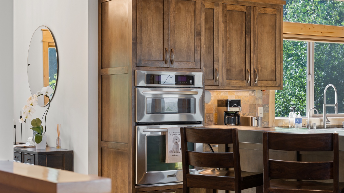 Gather around your fully-equipped kitchen, where rich wood cabinetry and modern stainless appliances make meal prep a breeze. Large windows frame lush greenery, bringing natural light into your vacation home.