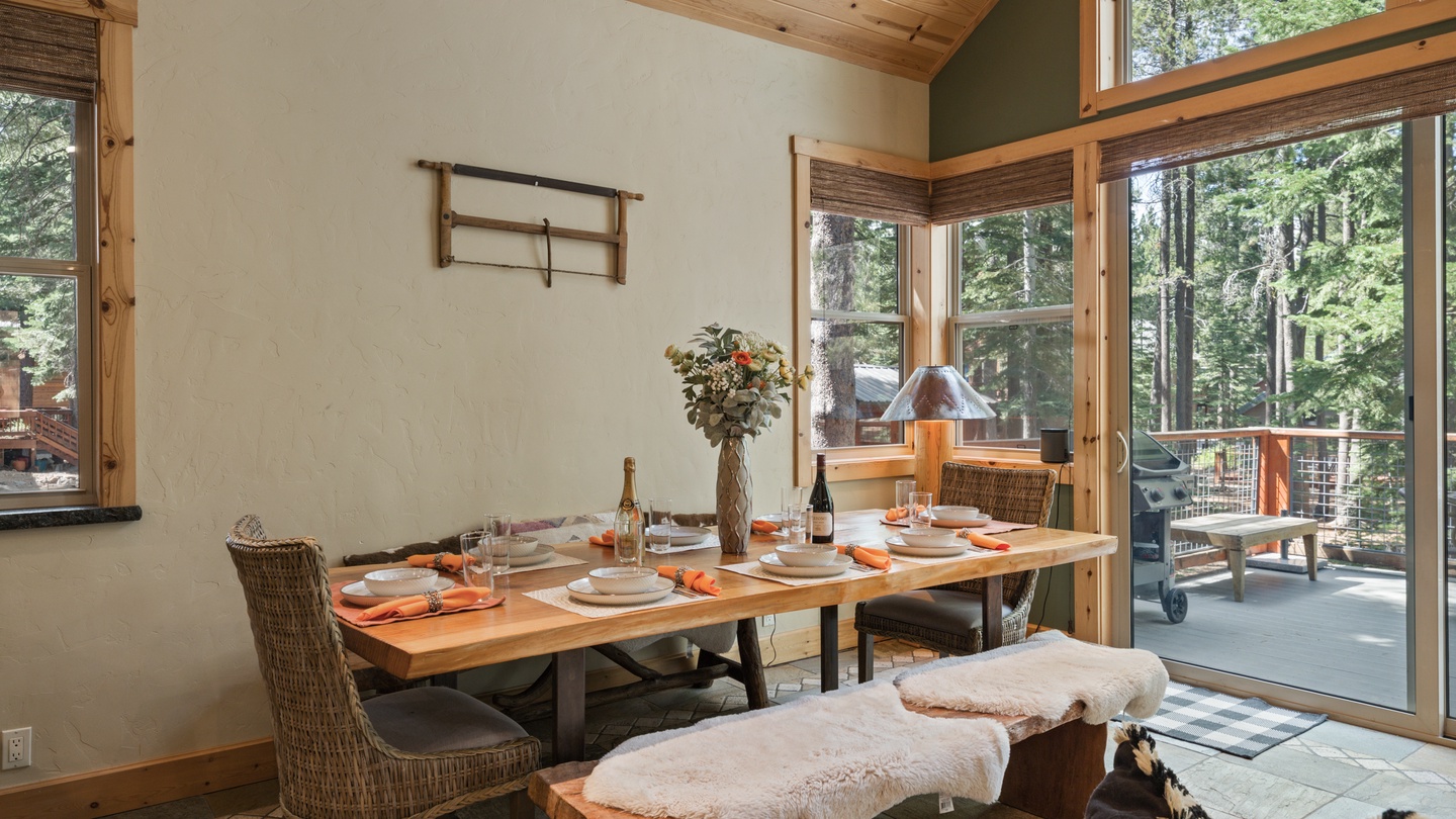 Gather around this inviting dining table with towering forest views through floor-to-ceiling windows. The warm wood ceiling and natural light create the perfect setting for your memorable meals together.