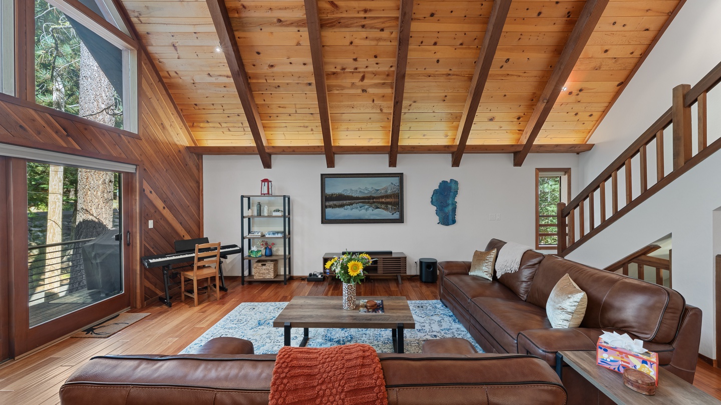 Sink into plush leather seating under soaring wood-beamed ceilings. Natural light floods through towering windows, inviting you to unwind in your private mountain escape with forest views just beyond the glass.
