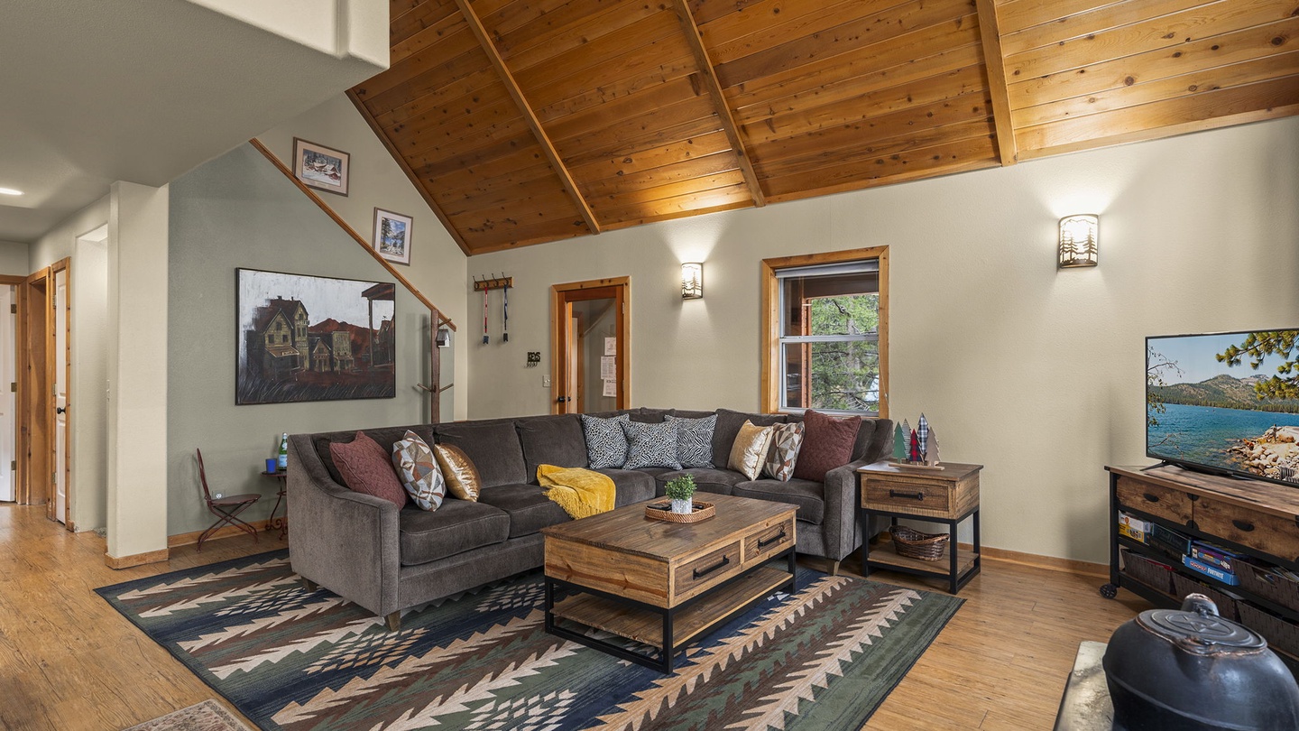 Sink into plush sectional seating beneath soaring wood-beamed ceilings where natural light streams through windows, creating your perfect mountain retreat sanctuary.