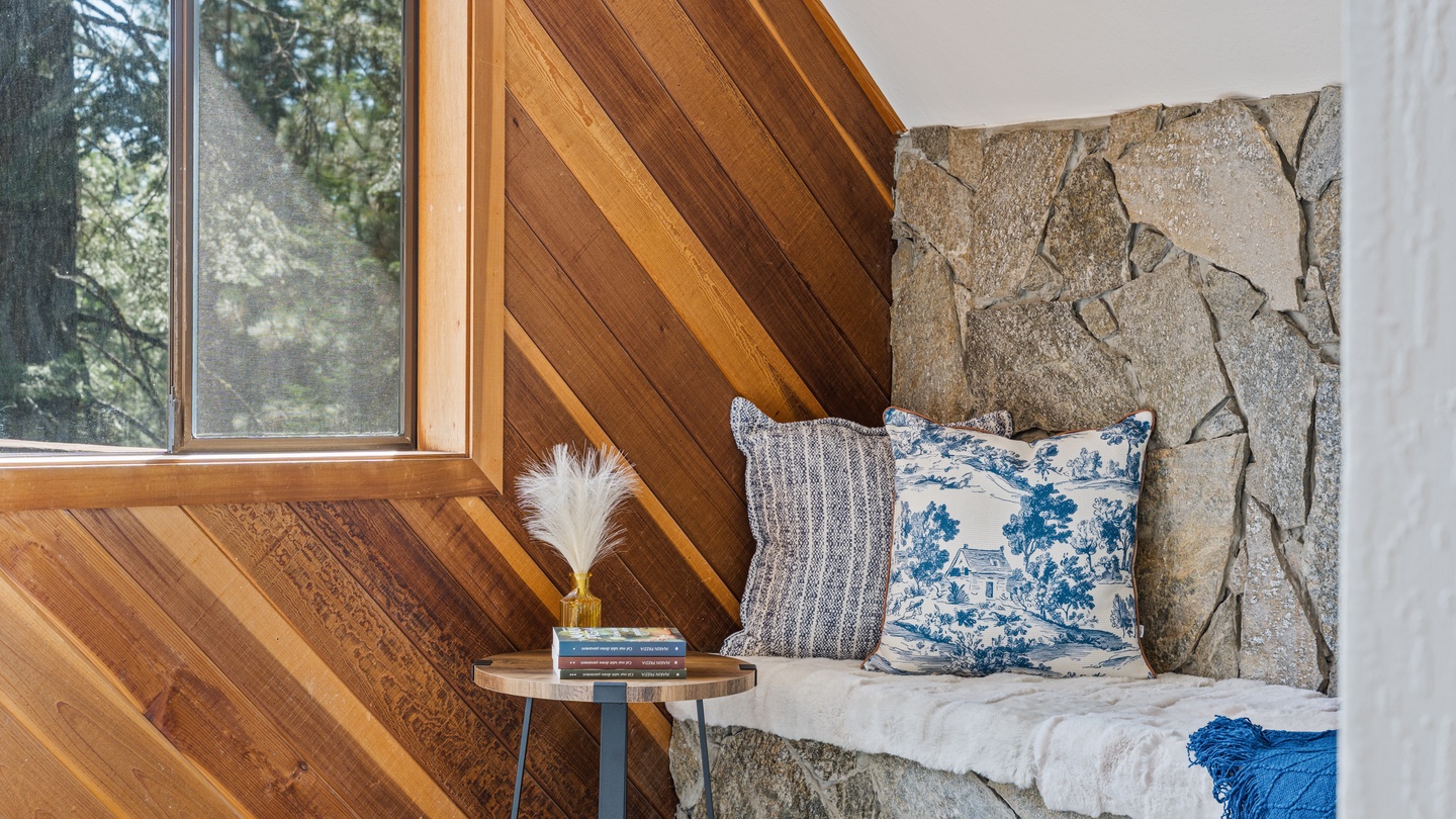 Curl up in this cozy reading nook where warm wood meets natural stone, with forest views inviting you to unwind with a good book and soft pillows.