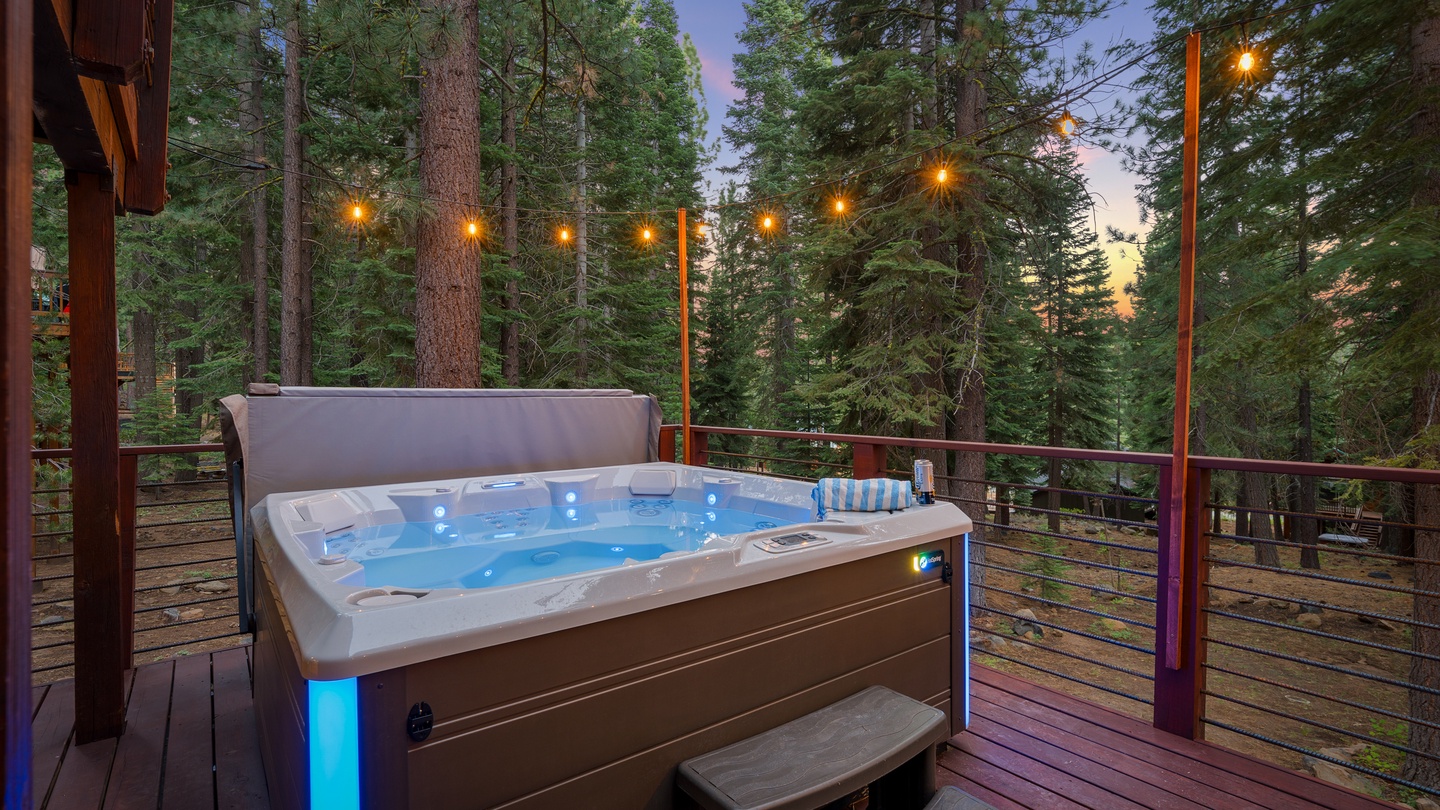 Slip into your private hot tub surrounded by towering pines, with glowing string lights overhead creating the perfect evening ambiance for relaxation.