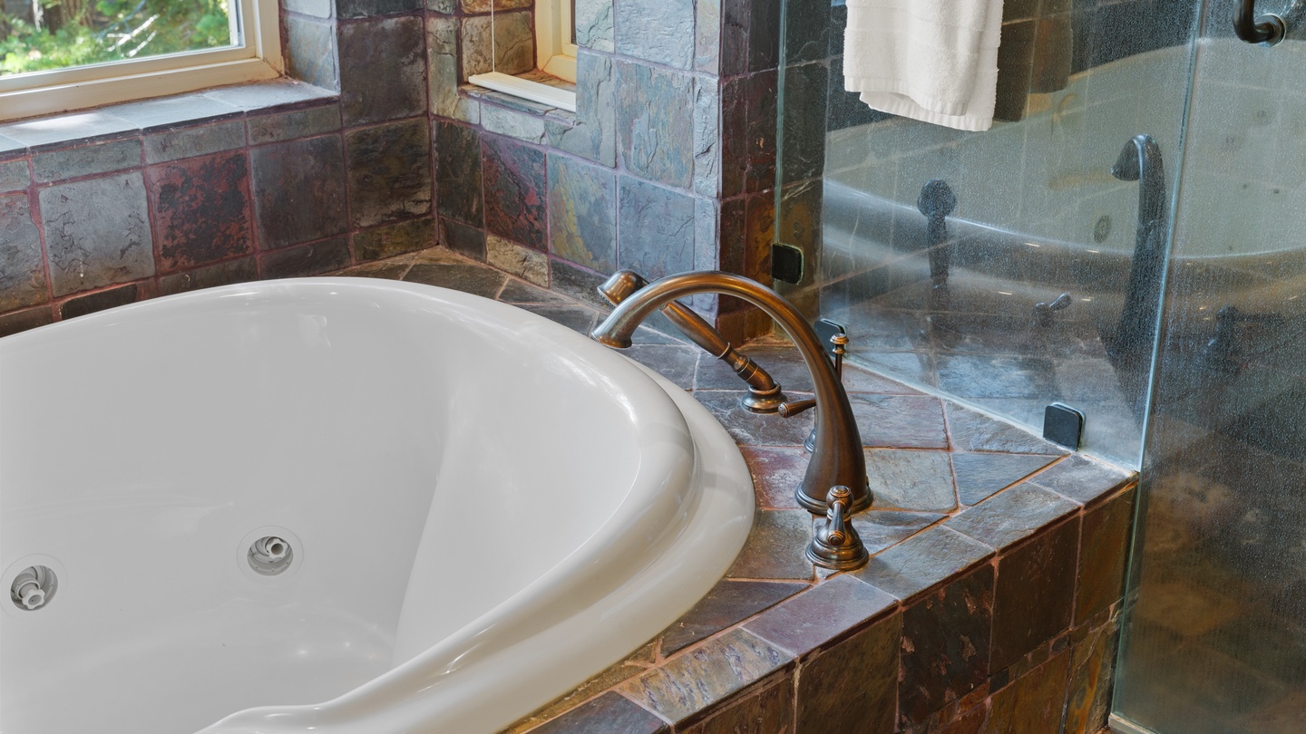 Soak your cares away in this elegant jetted tub, surrounded by rustic slate tile and natural light from the window. A steamy shower awaits behind the glass.