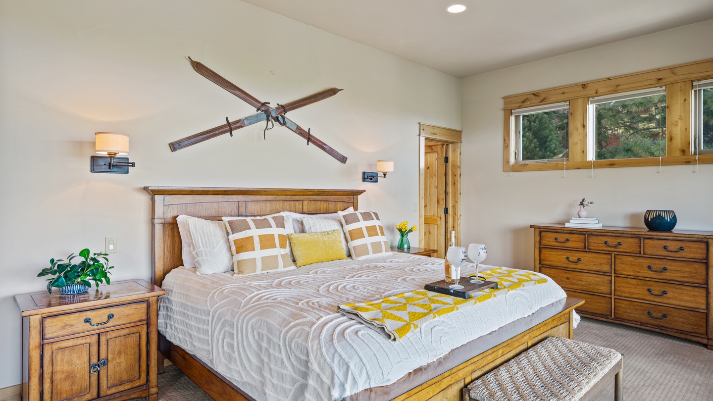Your spacious bedroom features warm wooden accents and a cozy king-size bed dressed in plush linens. Natural light floods in through the windows, while a ceiling fan keeps you comfortable year-round.