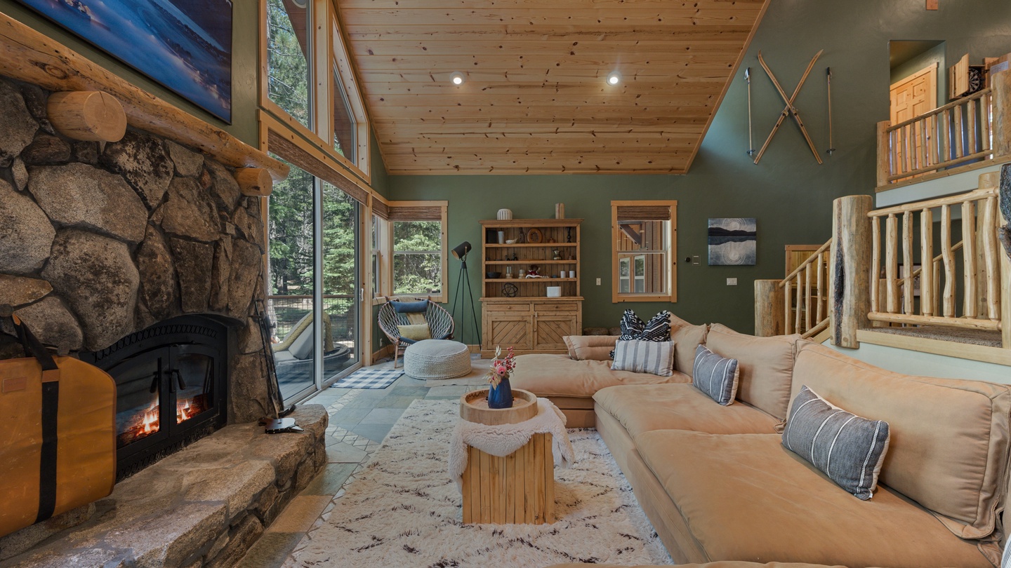 Sink into the plush sectional and let the warmth of the stone fireplace wrap around you while natural light pours through soaring windows, inviting the forest inside.