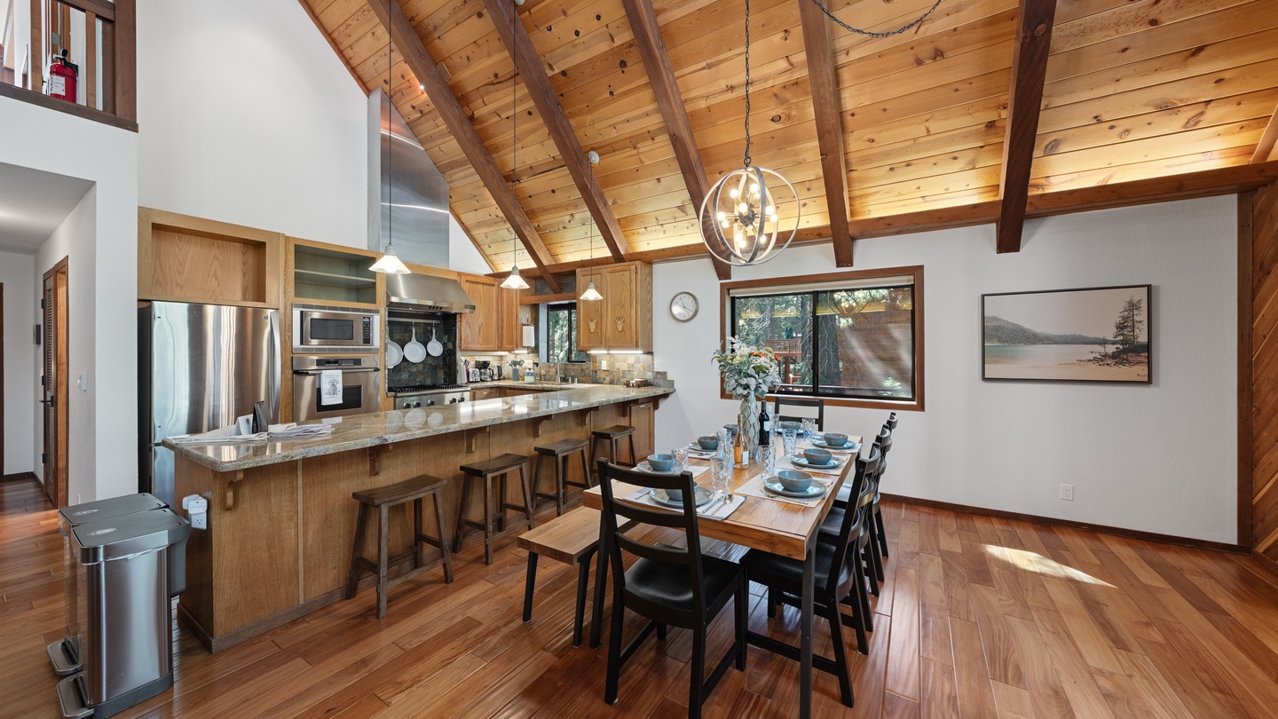 Your open-concept kitchen and dining area features warm wood floors, vaulted ceilings with exposed beams, and a breakfast bar for casual meals. Sunlight streams through the windows, illuminating a space perfect for gathering.