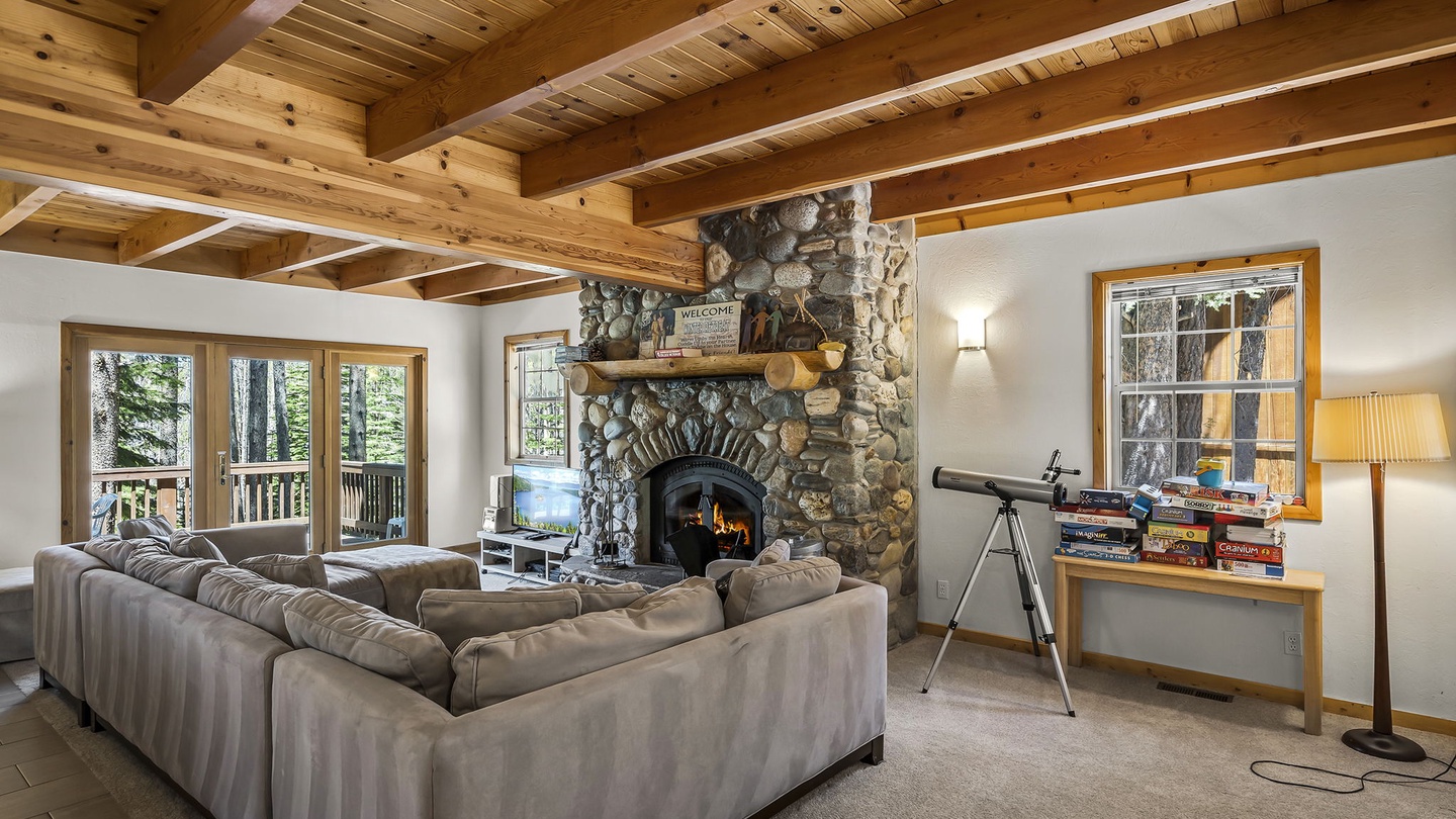 Sink into plush sofas beneath soaring wood beams, where a glowing stone fireplace sets the stage for cozy evenings. Natural light spills in through tall windows, inviting you to unwind with board games and your favorite books.