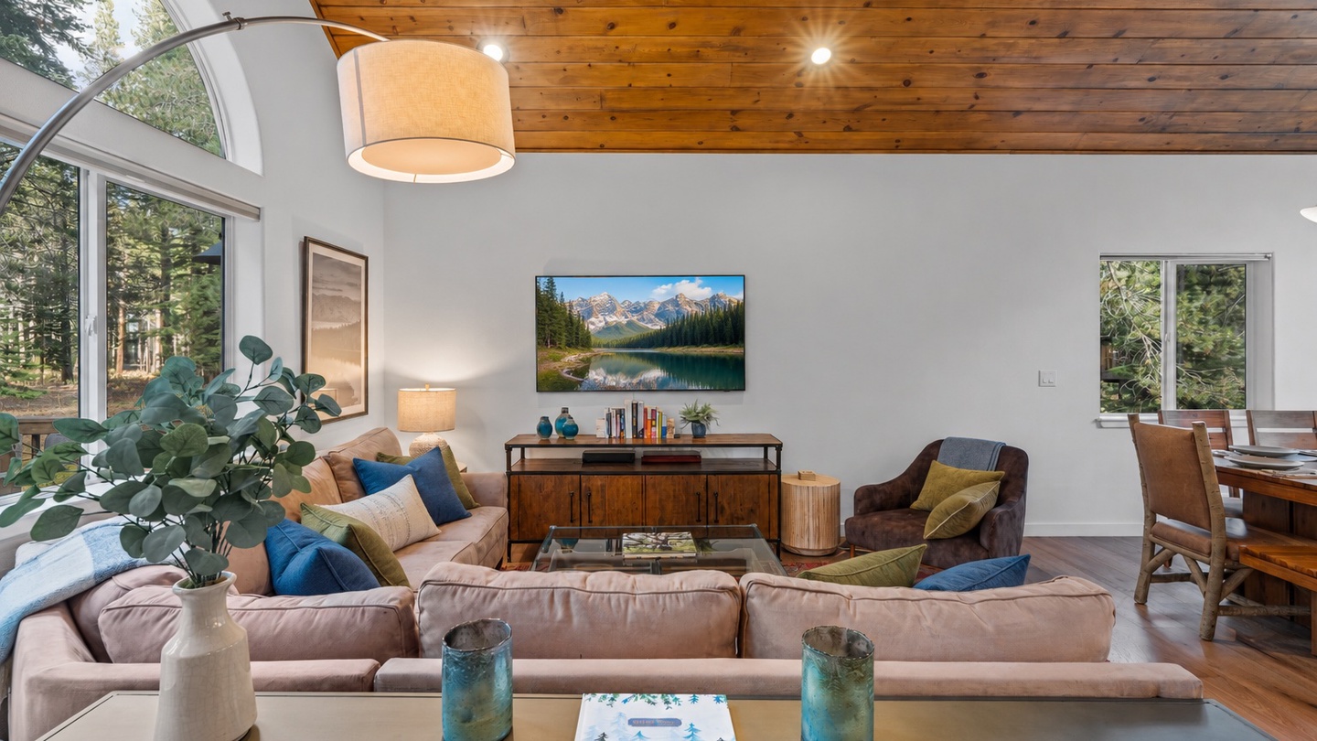 Relax in your open-concept living room with soaring wood ceilings, plush seating, and large windows framing the surrounding trees. Your perfect mountain retreat awaits.