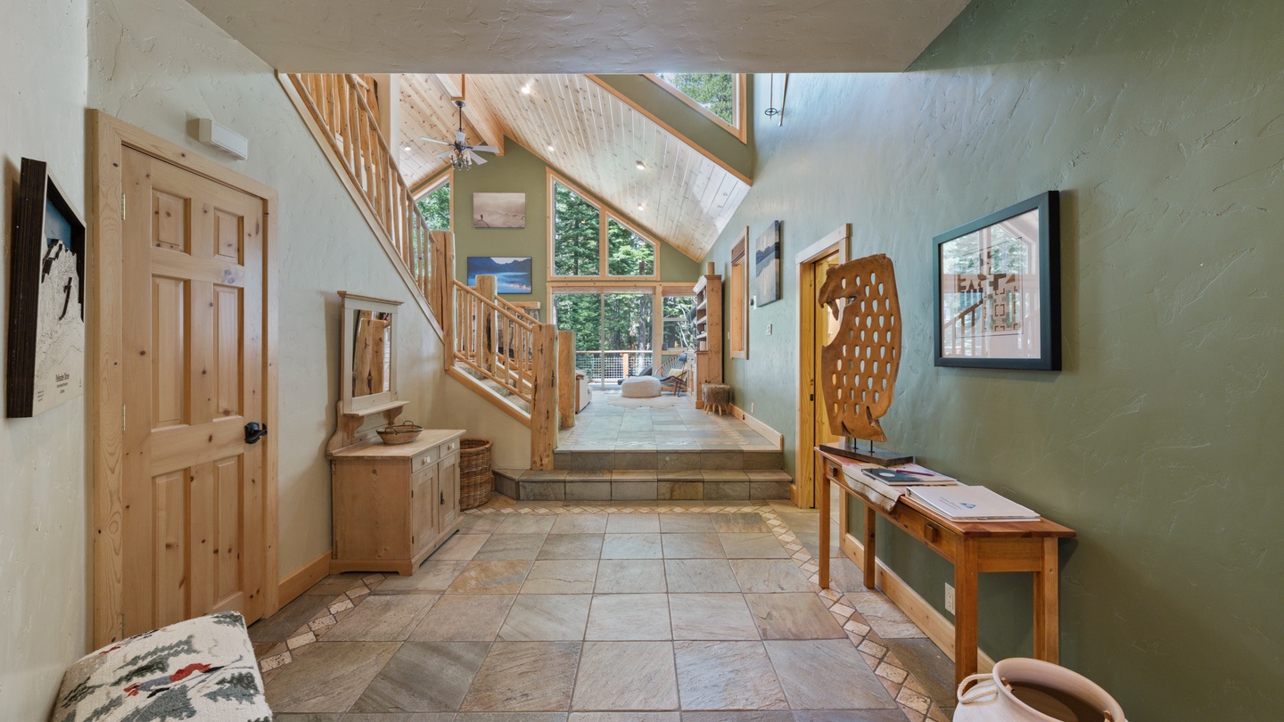 A welcoming entryway with vaulted ceilings and warm wood accents sets a relaxing tone as you arrive. Natural light pours through the windows, highlighting the spacious design and cozy seating area just beyond.