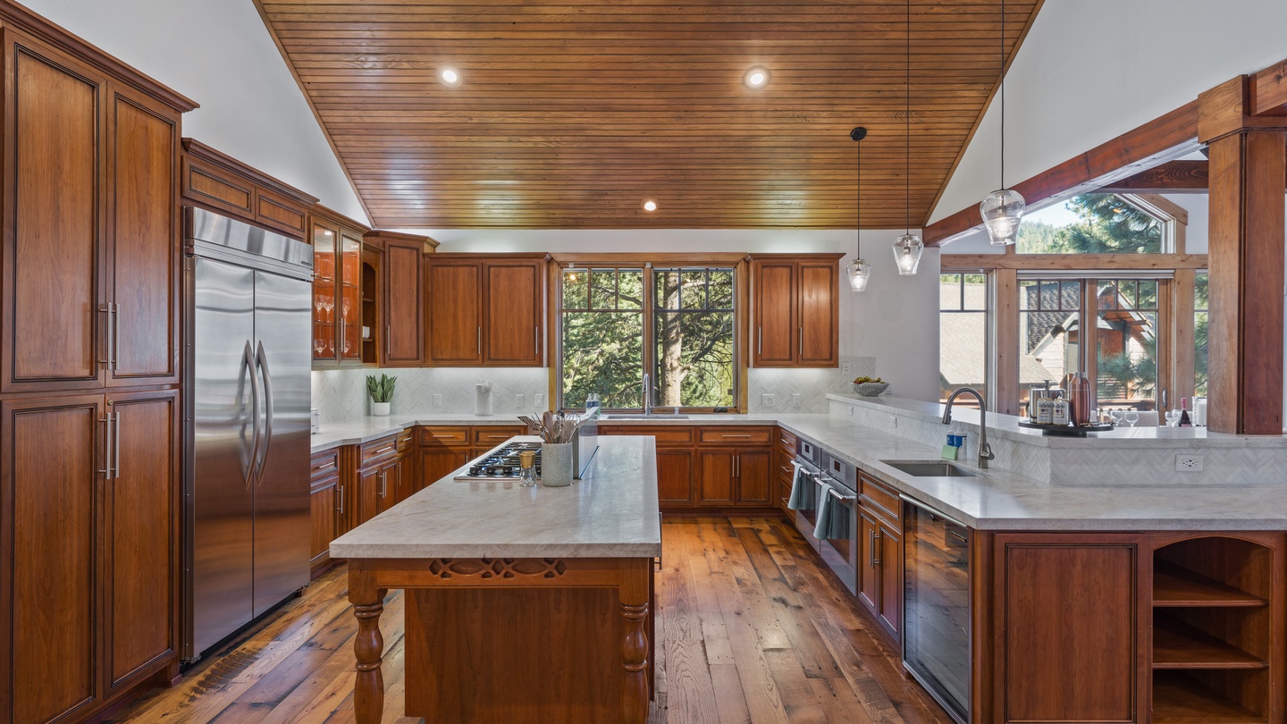 This spacious gourmet kitchen features rich hardwood cabinetry, gleaming marble countertops, and a stylish wood-paneled ceiling. Natural light streams through large windows, creating a warm and inviting space for your culinary adventures.
