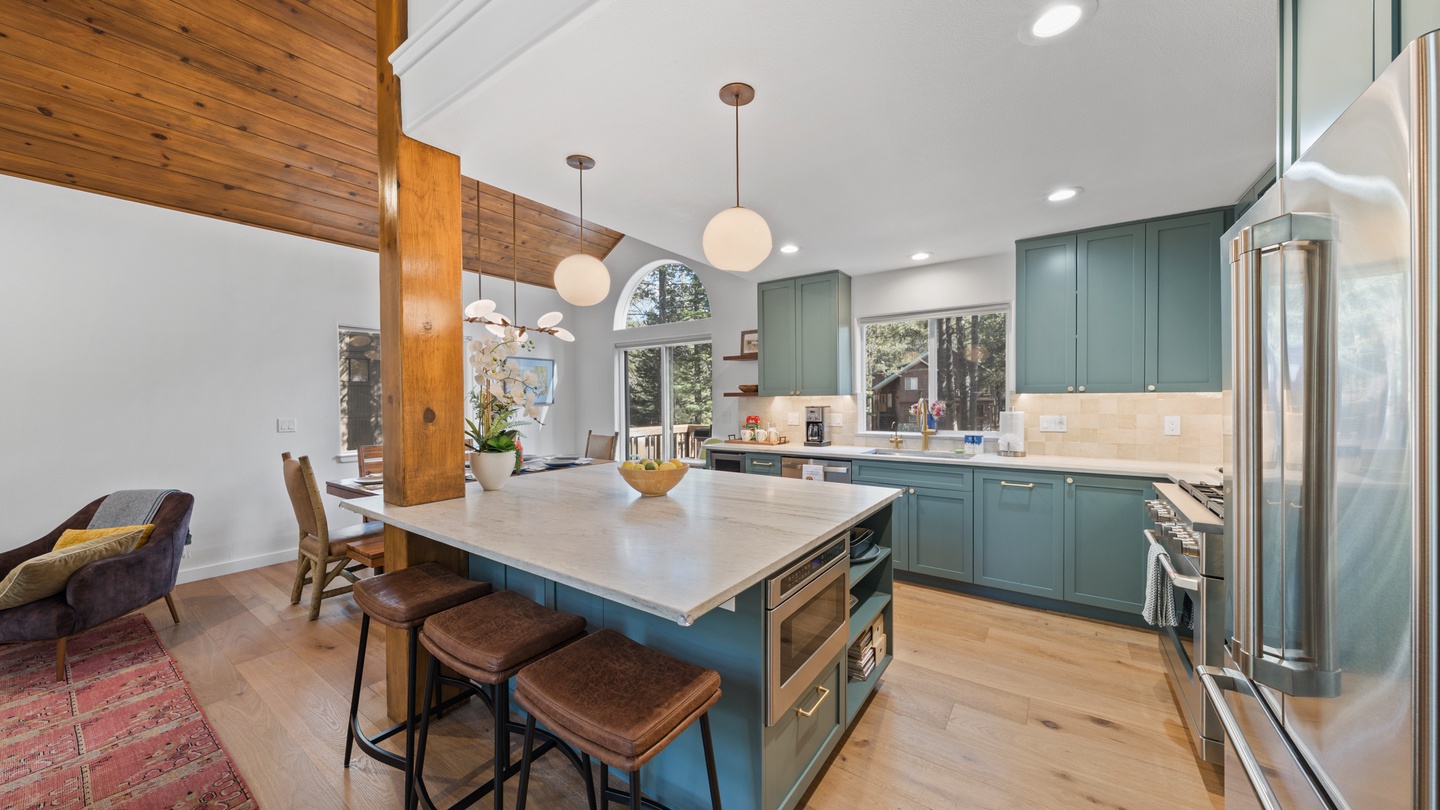 Stunning kitchen island with warm wood and marble, teal cabinetry, and soaring ceilings. Flooded with natural light, it features stainless appliances and thoughtful design ideal for cooking and gathering.