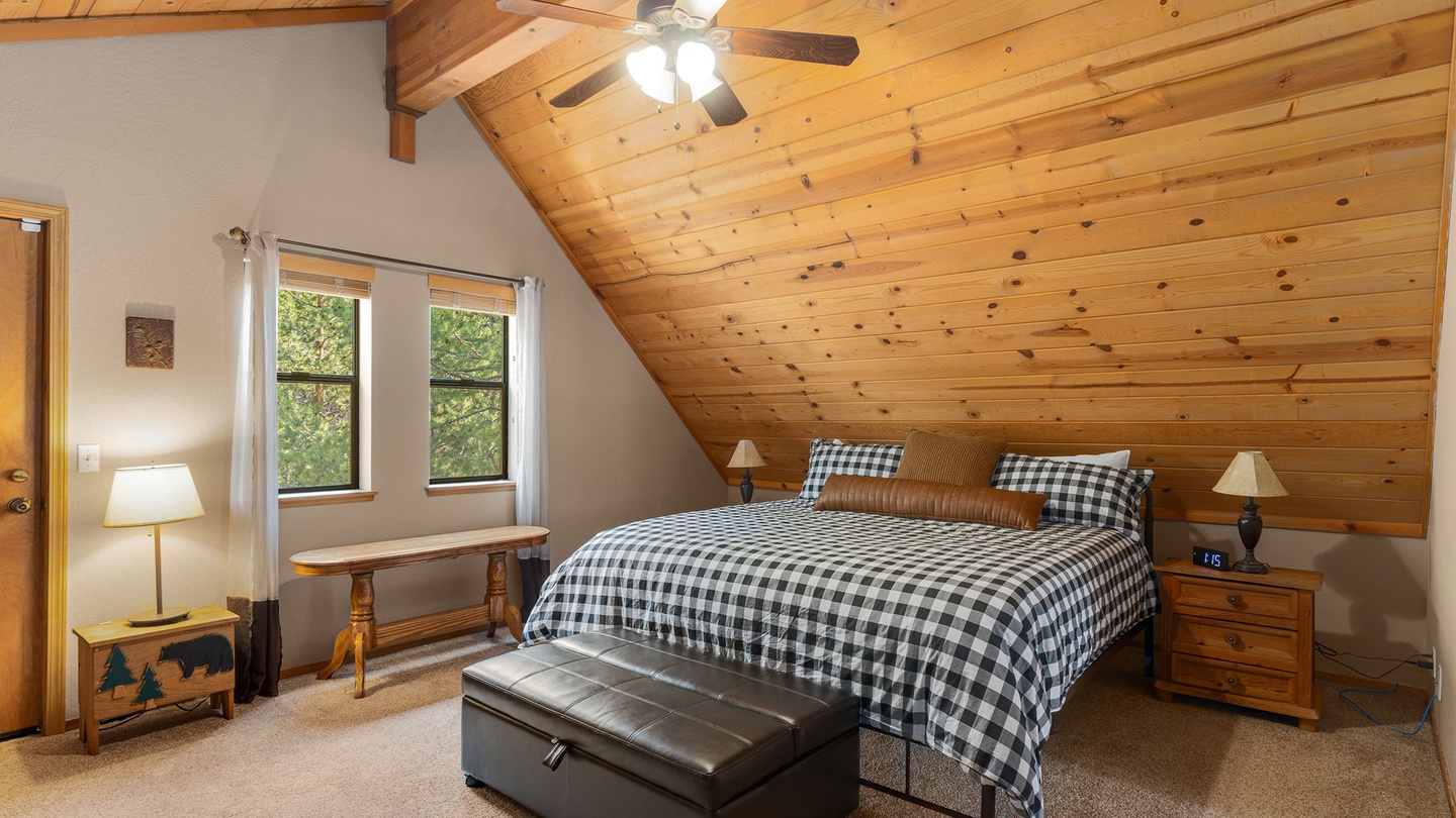 Unwind in your cozy cabin bedroom, wrapped in warm wood from floor to vaulted ceiling. Natural light filters through the windows, inviting you to relax on the plush bed after a day of adventure.