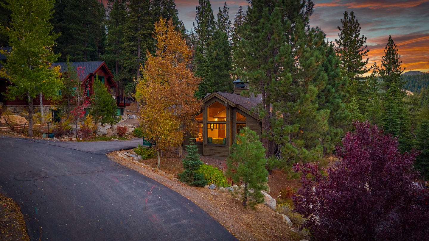 A welcoming mountain retreat framed by vibrant autumn foliage and towering pines, set against a stunning twilight sky as daylight fades into evening.