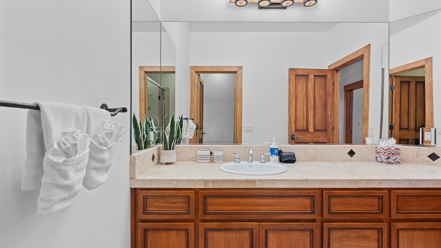 Freshen up in your beautifully appointed bathroom, featuring elegant wood cabinetry, a spacious vanity, and thoughtful touches like plush towels and a calming green plant.