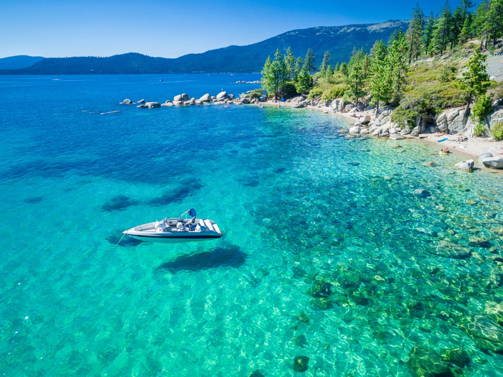 Crystal-clear alpine lake with pristine shoreline, surrounded by forested mountains and granite boulders.