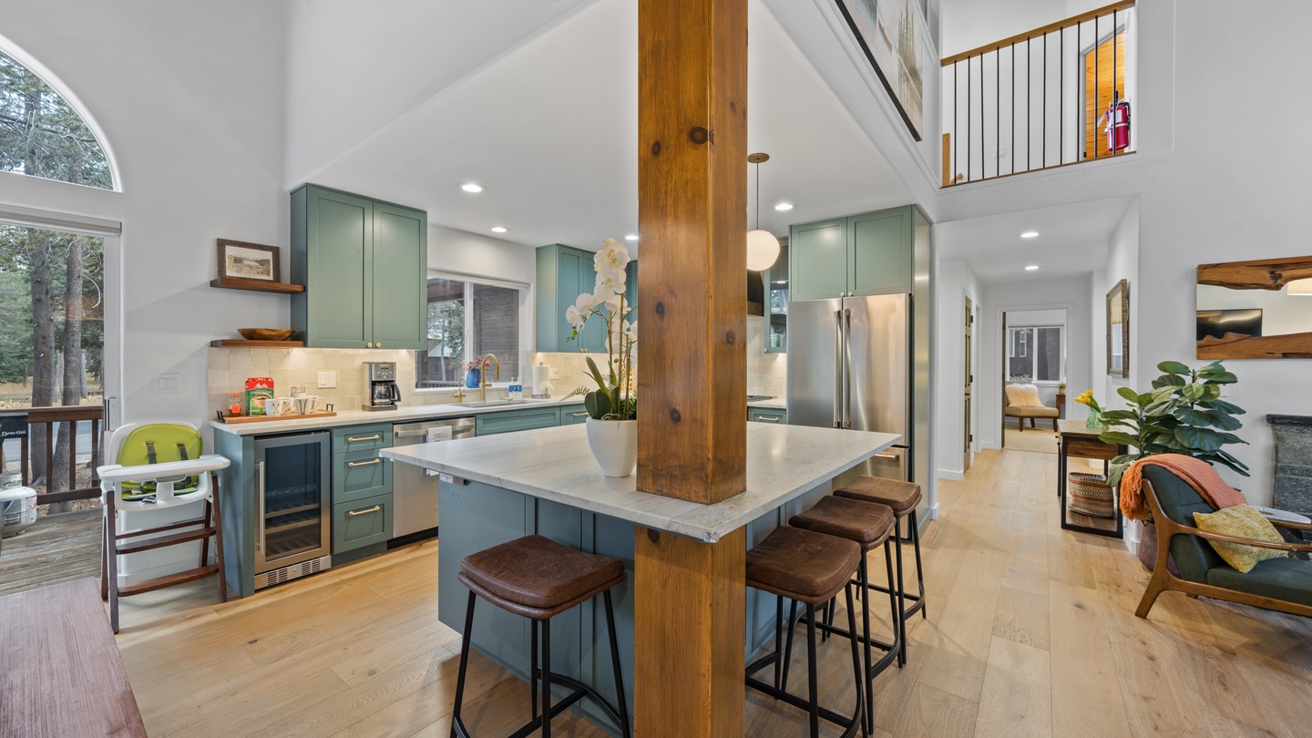 Step into your open-concept haven where soaring ceilings and rich wood beams create a sense of spaciousness. The well-appointed kitchen features modern teal cabinetry and a central island perfect for gathering with loved ones.