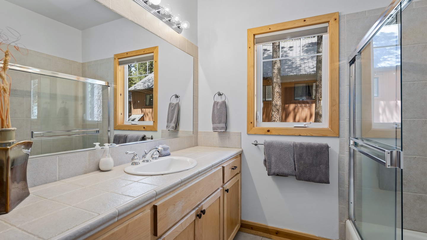 Refresh in your modern bathroom featuring a soaking tub and walk-in shower with natural light from charming wood-framed windows overlooking the trees.