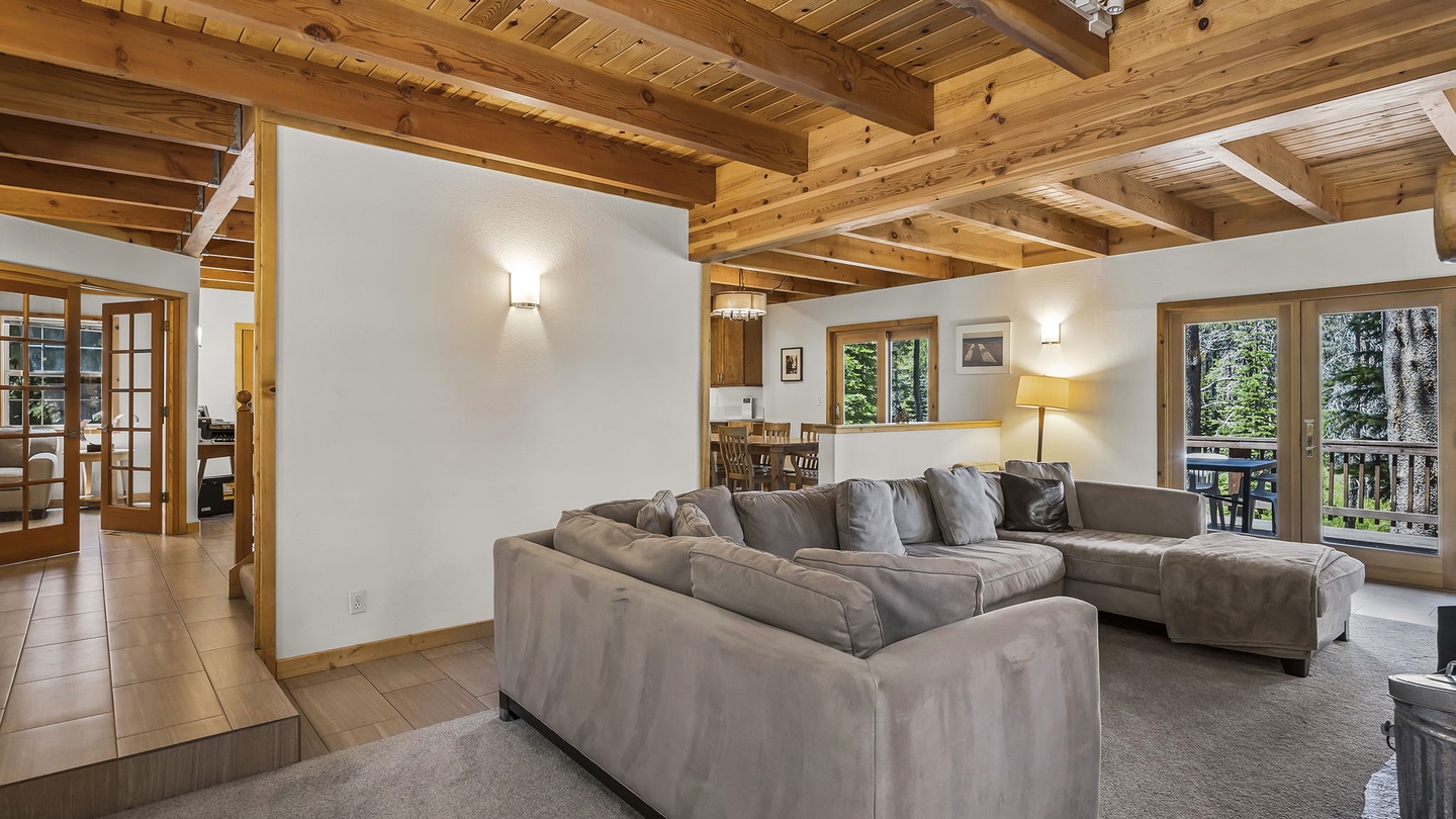 Sink into plush seating beneath warm wood beams as natural light streams through the windows, framing your forest retreat just beyond the deck.
