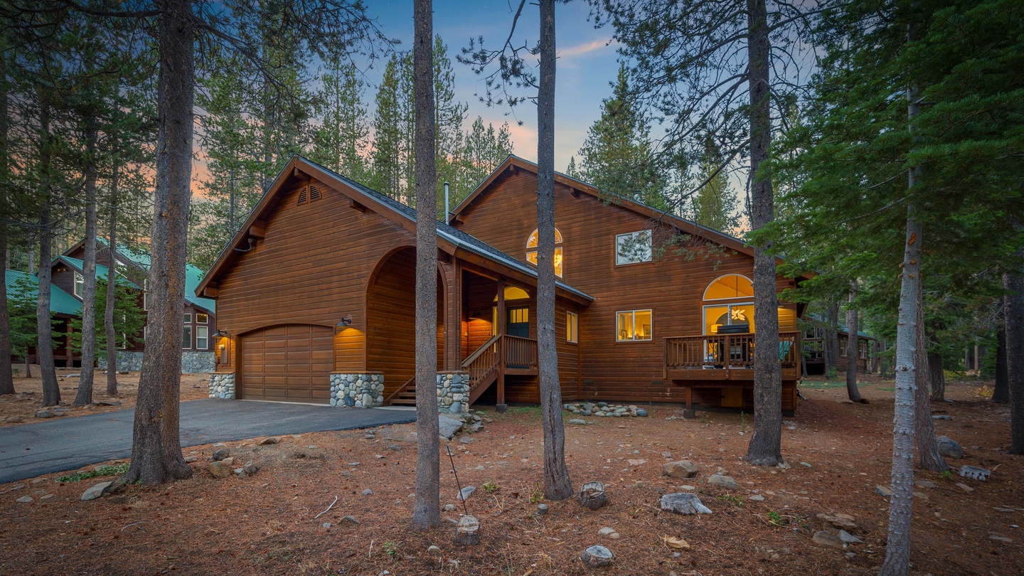 A charming mountain cabin nestled among towering pines, featuring warm wood siding, stone accents, and glowing windows that welcome guests to their peaceful forest retreat.