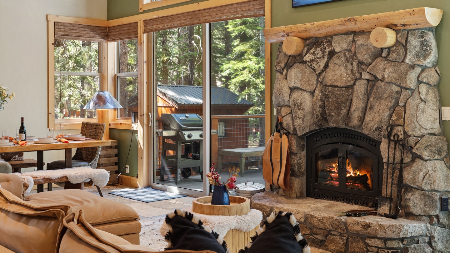 Sink into plush seating as the crackling stone fireplace warms your retreat, while forest views through expansive windows invite the outdoors in.