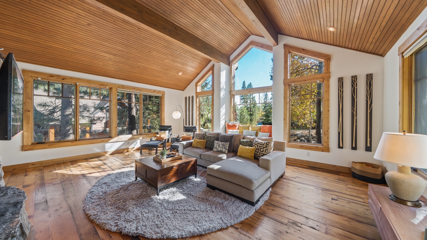 Picture yourself unwinding in this sun-drenched living room, where soaring wood ceilings and floor-to-ceiling windows frame views of the surrounding forest. Sink into the cozy sectional and let natural light warm your stay.